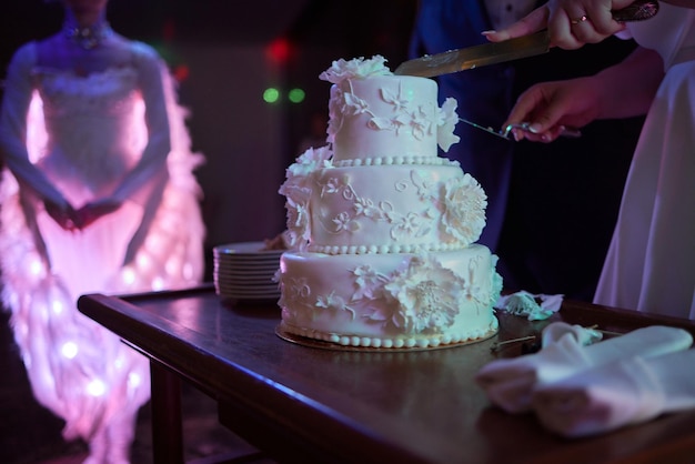 La mariée et le marié au banquet coupent ensemble le gâteau de mariage en tenant un couteau Détails du mariage en gros plan