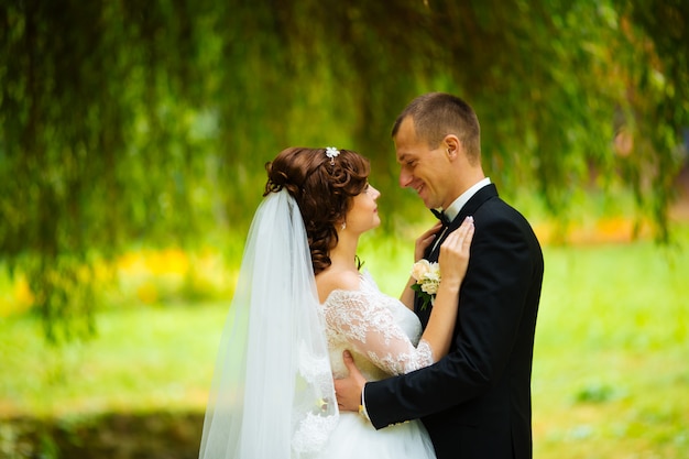 Mariée et le marié au jour du mariage en marchant à l'extérieur sur la nature d'automne. Couple nuptial, heureux jeune femme et homme embrassant dans un parc verdoyant. Couple de mariage aimant en plein air.