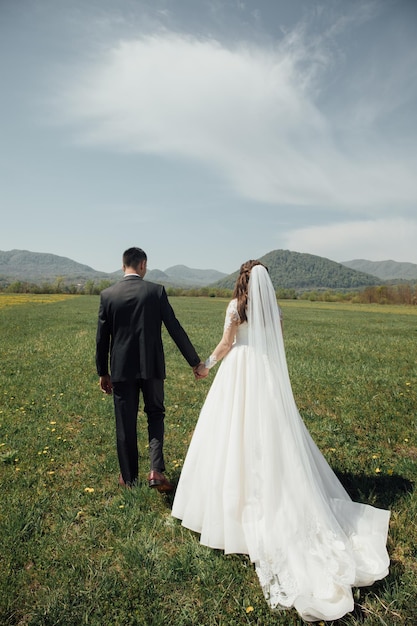 Mariée et le marié au jour du mariage marchant à l'extérieur sur la nature verte d'été.