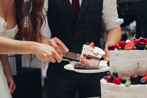 Mariée et le marié coupe le gâteau de mariage morceau de dessert sucré délicieux. Concept de confiserie, de célébration et d'amour.