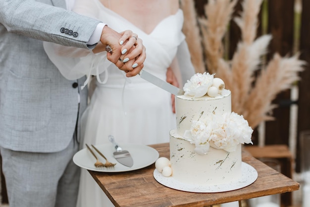 La mariée et le marié coupent leur beau gâteau de mariage lors d'un banquet de mariage Les mains coupent le gâteau avec de délicates fleurs blanches