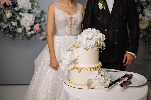 La mariée et le marié coupent leur gâteau de mariage rustique lors d'un banquet de mariage Les mains coupent le gâteau avec de délicates fleurs roses