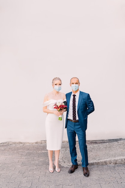 Mariée et marié dans des masques médicaux sur fond gris. Mariage pour deux pendant l'isolement, Covid-19