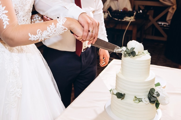 La mariée et le marié à la fin de la fête de mariage ont coupé le gâteau de mariage. Jeune couple heureux a coupé un gâteau à la fin d'une journée de mariage. Gâteau de mariage de luxe.