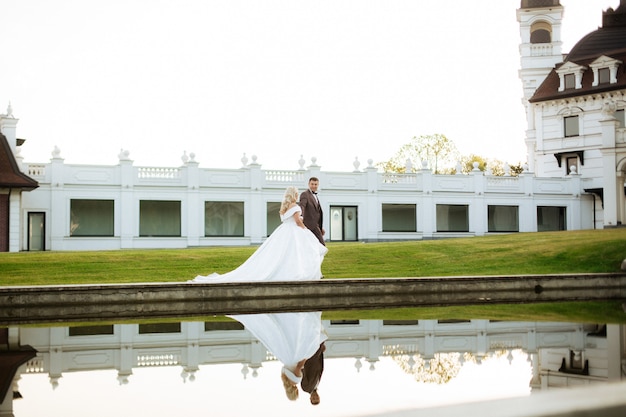 La mariée et le marié marchent ensemble dans le parc. Charmante mariée dans une robe blanche, le marié est vêtu d'un costume sombre et élégant