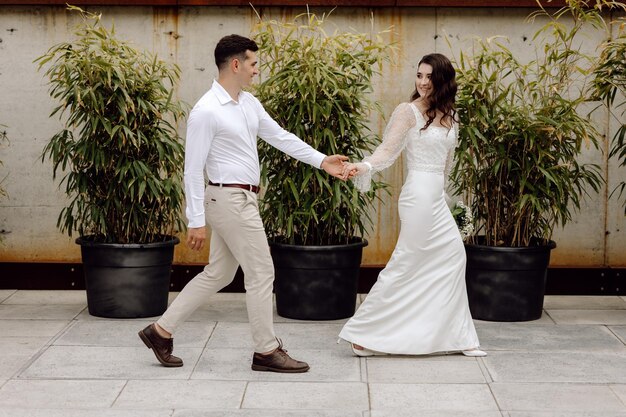 Une mariée et un marié marchent main dans la main devant des bambous.