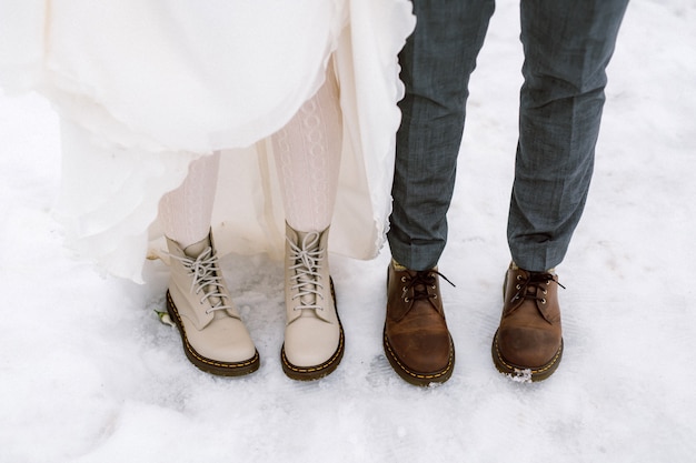 Mariée et le marié portant des bottes, debout sur la neige