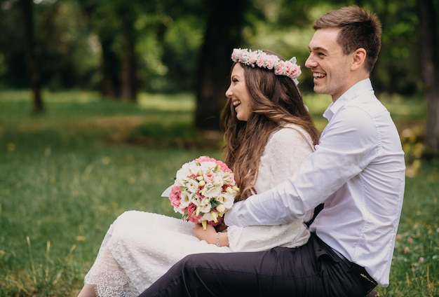 Une mariée et un marié s'assoient sur un banc dans un parc