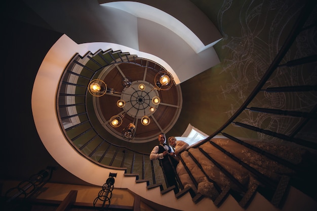 La mariée et le marié s'embrassant et s'étreignant sur un escalier en colimaçon. Portrait d'aimer les jeunes mariés dans un bel intérieur. Jour de mariage. concept de mariage. tout juste marié. couple de mariage amoureux à l'intérieur