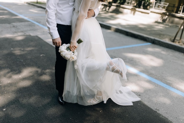 Photo la mariée et le marié s'embrassent dans la rue. la mariée tient un bouquet blanc et a levé la jambe