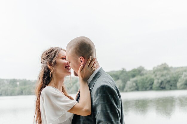 La mariée et le marié s'embrassent sur le rivage du lac.