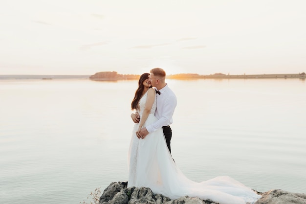 Une mariée et un marié s'embrassent sur un rocher devant un lac.