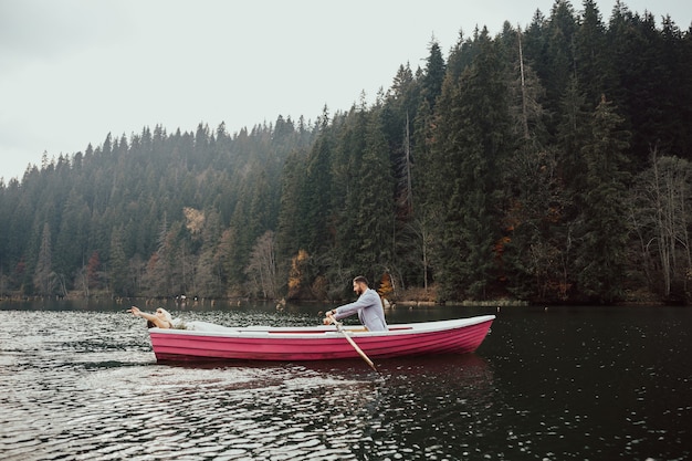 La mariée et le marié sont assis ensemble dans un petit bateau rose sur le lac. Le mari fait rouler sa femme sur le bateau.