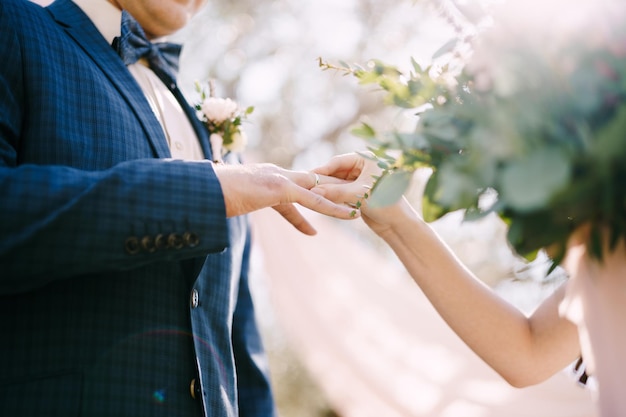 La mariée met la bague au doigt du marié dans le parc en gros plan