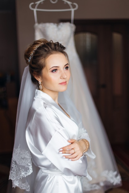 Mariée en peignoir blanc avec maquillage et voile de mariée bras croisés