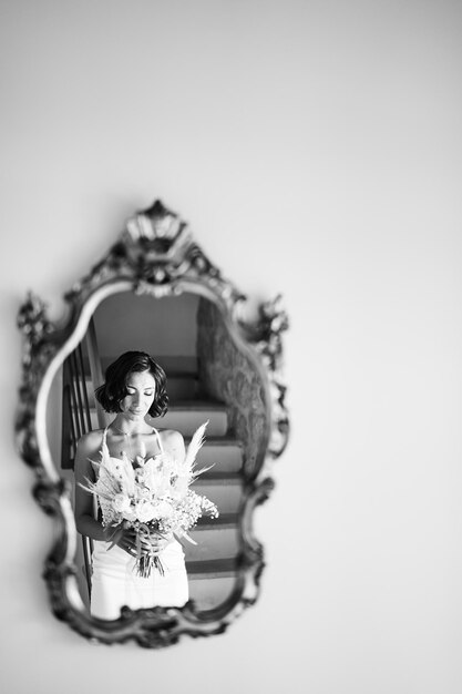 Photo la mariée regarde un bouquet de fleurs dans ses mains reflété dans le miroir sur le mur noir et blanc