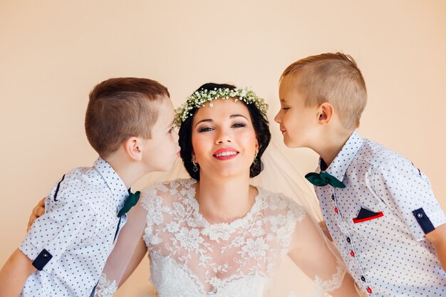 La mariée regarde la caméra et sourit, les petits garçons veulent embrasser la mariée sur les joues