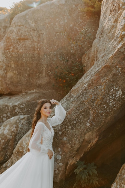 Mariée en robe blanche debout sur la colline et regardant le coucher du soleil.