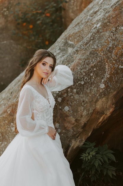 Mariée en robe blanche debout sur la colline et regardant le coucher du soleil.