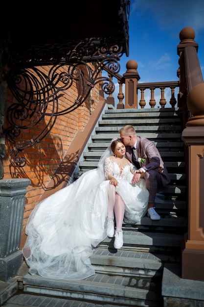 La mariée en robe blanche et le marié en costumes s'embrassent sur les marches