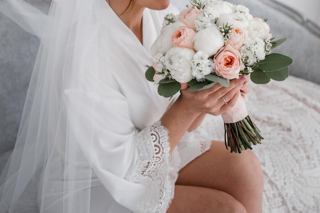 la mariée en robe blanche le matin tient un bouquet dans ses mains