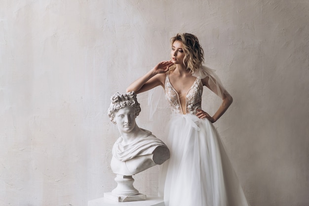 Mariée en robe blanche s'appuyant sur la sculpture. portrait de la belle mariée en robe de mariée blanche avec décolleté. robe de mariée avec décolleté orné de dentelle