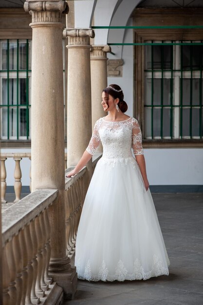 Une mariée en robe blanche se tient devant un balcon