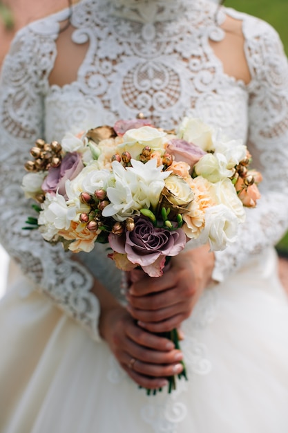 Mariée en robe blanche tenant un bouquet de fleurs blanches et de verdure. Roses blanches, violettes, roses.