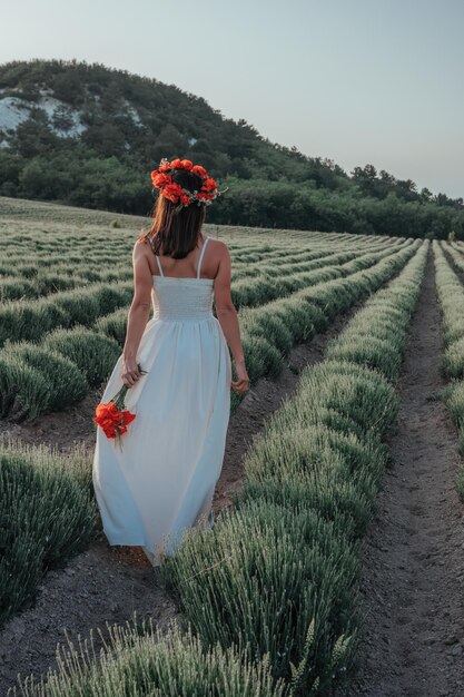 Mariée en robe blanche tenant un bouquet de fleurs de pavot heure du coucher du soleil chaud sur le fond de la