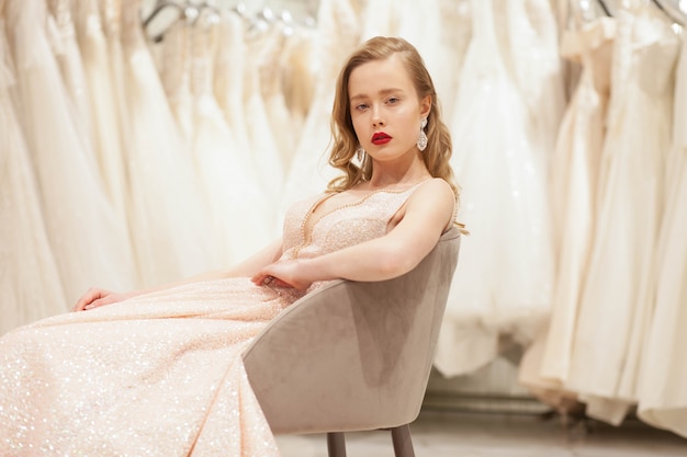 Mariée en robe chic posant sur une chaise dans un salon de mariage