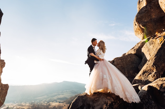 Mariée en robe élégante avec dentelle et marié en costume sur fond de falaises et de montagnes