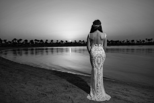 Mariée robe de mariée blanche debout sur la plage de sable robe de mariée mariée heureuse profiter du coucher du soleil fond de l'océan