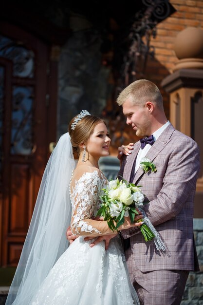 La mariée en robe de mariée blanche et le marié en costume sur le fond d'un immeuble en briques avec de grandes marches