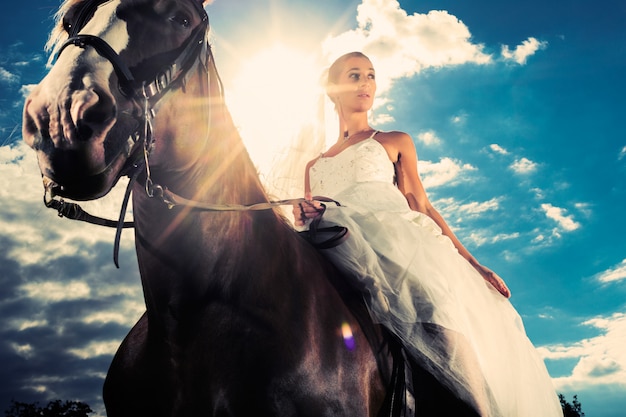 Mariée en robe de mariée à cheval, rétro-éclairé