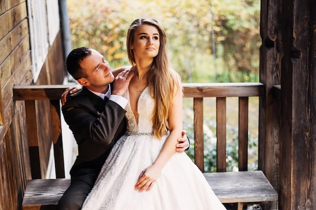 La mariée en robe de mariée est assise avec le marié en uniforme sur un banc près de