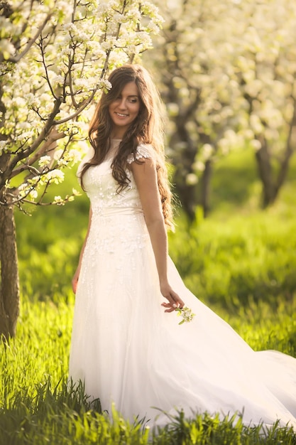 Mariée en robe de mariée ivoire avec de longs cheveux bouclés marchant dans des jardins de printemps avec des arbres en fleurs