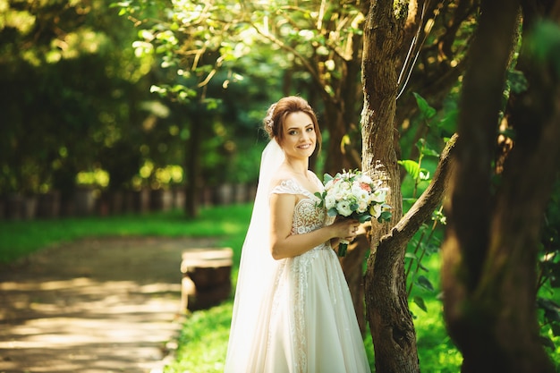 Mariée en robe de mariée de mode sur fond naturel. Un beau portrait de femme dans le parc