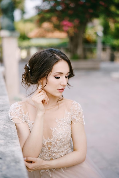 La mariée s'assied près d'une balustrade en pierre dans le portrait de jardin