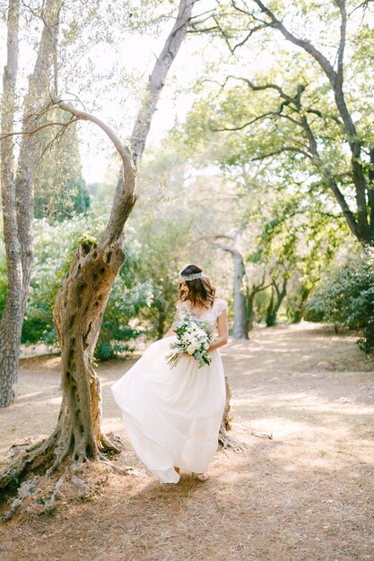 Photo la mariée se promène parmi les arbres dans un parc pittoresque et tient un bouquet dans ses mains