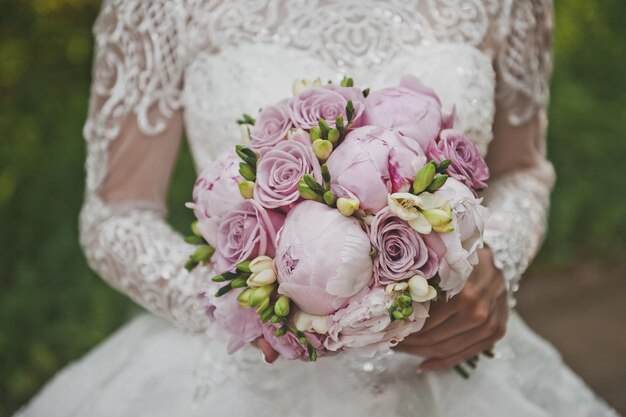 La mariée se tient dans le jardin et tient un bouquet de mariage lumineux de pivoines et de roses dans ses mains 2669