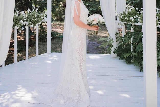 Une mariée se tient sur un porche avec son bouquet de fleurs.