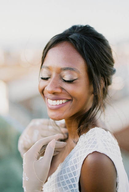 Une mariée souriante en gants touche ses clavicules avec son portrait de mains