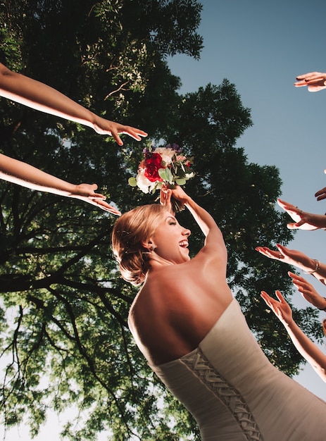 La mariée souriante jette le bouquet de mariage de ses amis