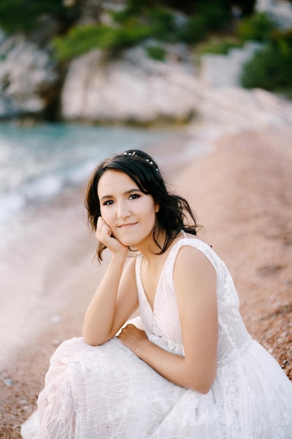 Mariée souriante en robe blanche assise sur la plage