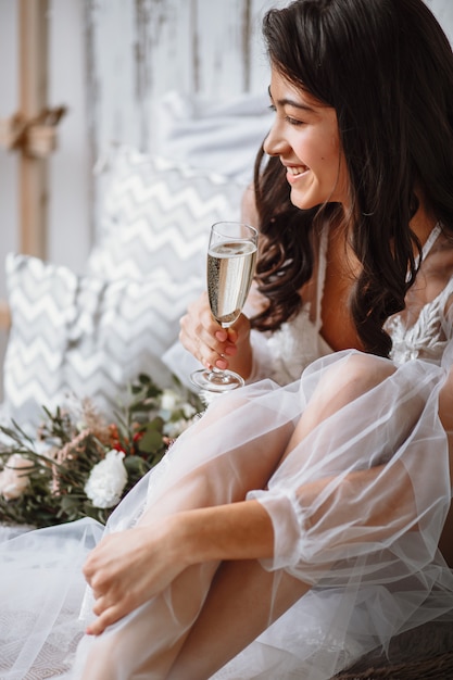 Mariée en sous-vêtements avec une coupe de champagne sur le lit