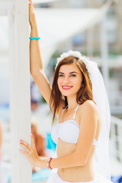 Mariée en soutien-gorge et voile de mariée. jeune femme sourit et détient behin