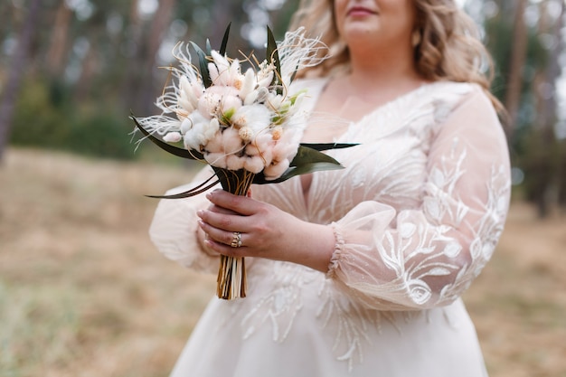 Photo mariée tient un bouquet de mariage de fleurs blanches et beiges à l'extérieur l bouquet de fête dans les mains de la femme