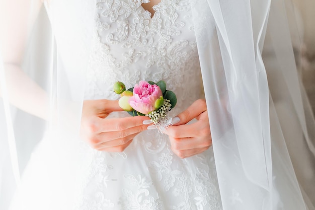 La mariée tient une boutonnière de mariage dans sa main Un bouquet de fleurs avec des pivoines pour le marié le jour du mariage