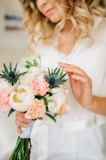 La mariée tient dans sa main et touche doucement un bouquet de pivoines, roses, lisianthus et