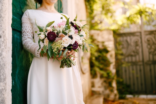 La mariée tient dans ses mains un beau bouquet de fleurs appuyé contre la porte verte de la